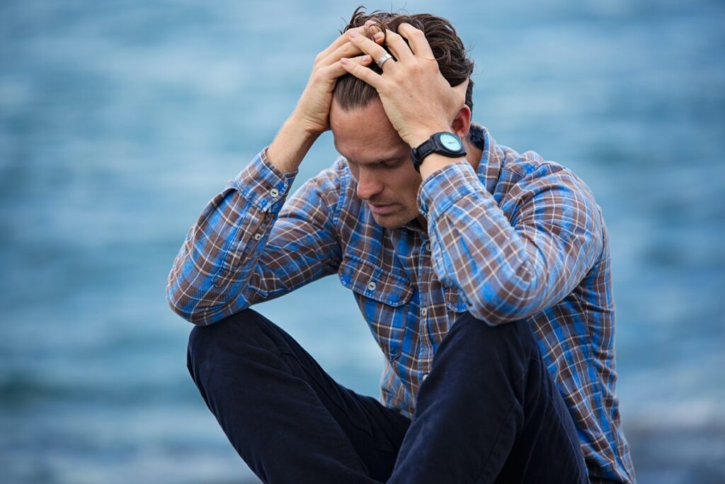 depressed man sitting down with his hands over his head 