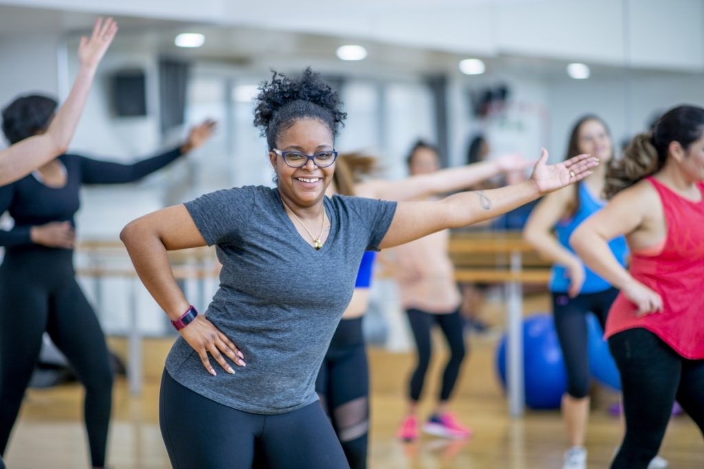A woman of african descent looks into the camera smiling while she dances during a fitness class