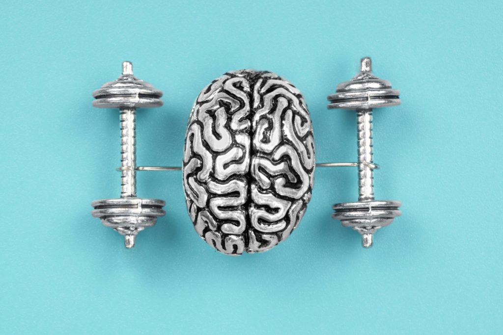 Creative composition made of a steel copy of a human brain lifting dumbbells. The concept of brain exercises to strengthen the mind.