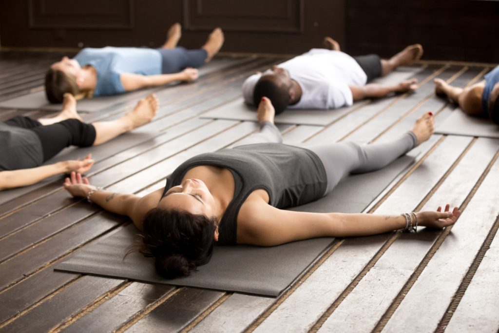 Group of young afro american and caucasian sporty people practicing yoga lesson lying in Dead Body pose, Savasana exercise, working out, resting after practice