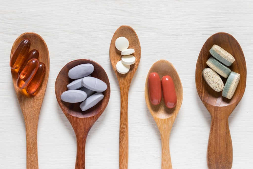 Variety of vitamin pills in wooden spoon on white background, supplemental and healthcare product, flat lay surfac