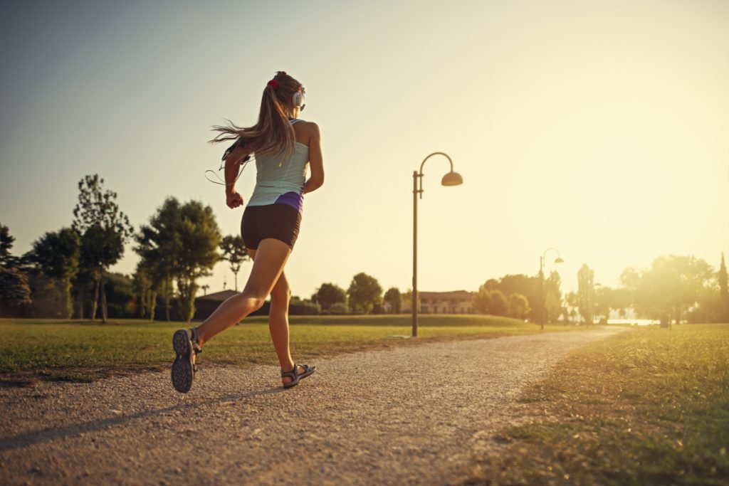 Teenage girl jogging in city park. Sunny summer day sunset.