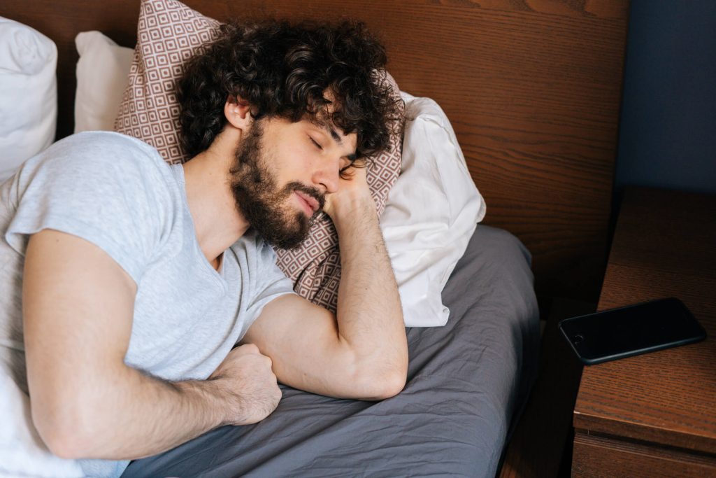 young man sleeping peacefully lying on side in large comfortable double bed